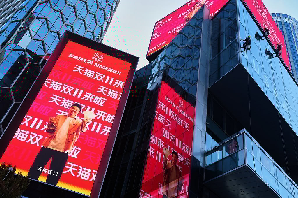 Window cleaners labor an commercial office as an advertisement billboard promoting Tmall's Singles' Day sale at a shopping district in Beijing on Nov. 10, 2025.