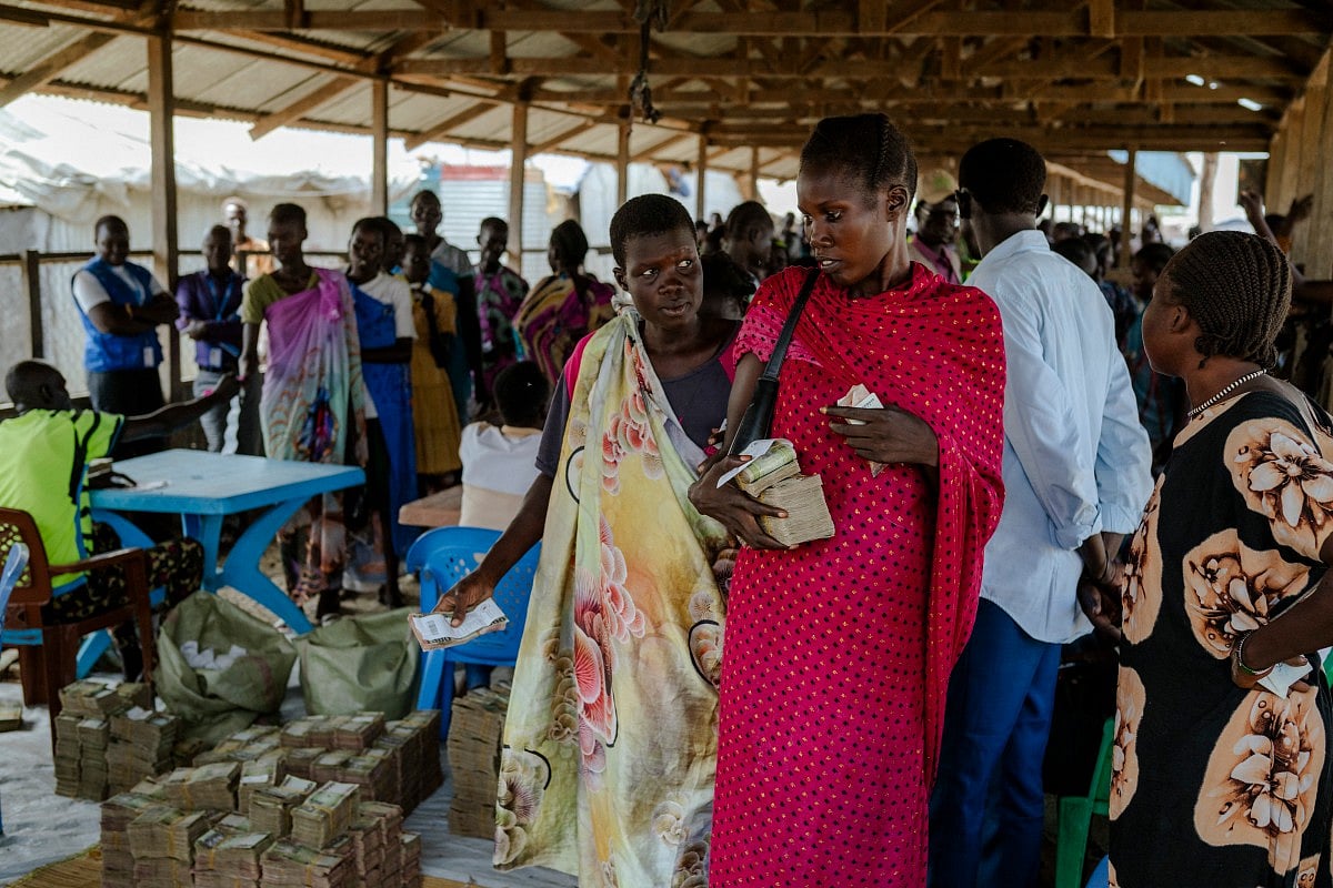 A woman observes with raised eyebrows as another woman holds a large bundle of South Sudanese pounds (SSP) during a cash-based transfer at a distribution center in the Bentiu internally displaced persons camp, Unity State, South Sudan, on November 6, 2025.