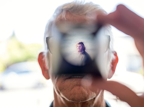 Christy Morrill, 72, who lost decades of memories to autoimmune encephalitis, holds up a viewfinder with a slide film of himself as a college student, Wednesday, Aug. 20, 2025, at his home in San Carlos, Calif. (AP Photo/David Goldman)