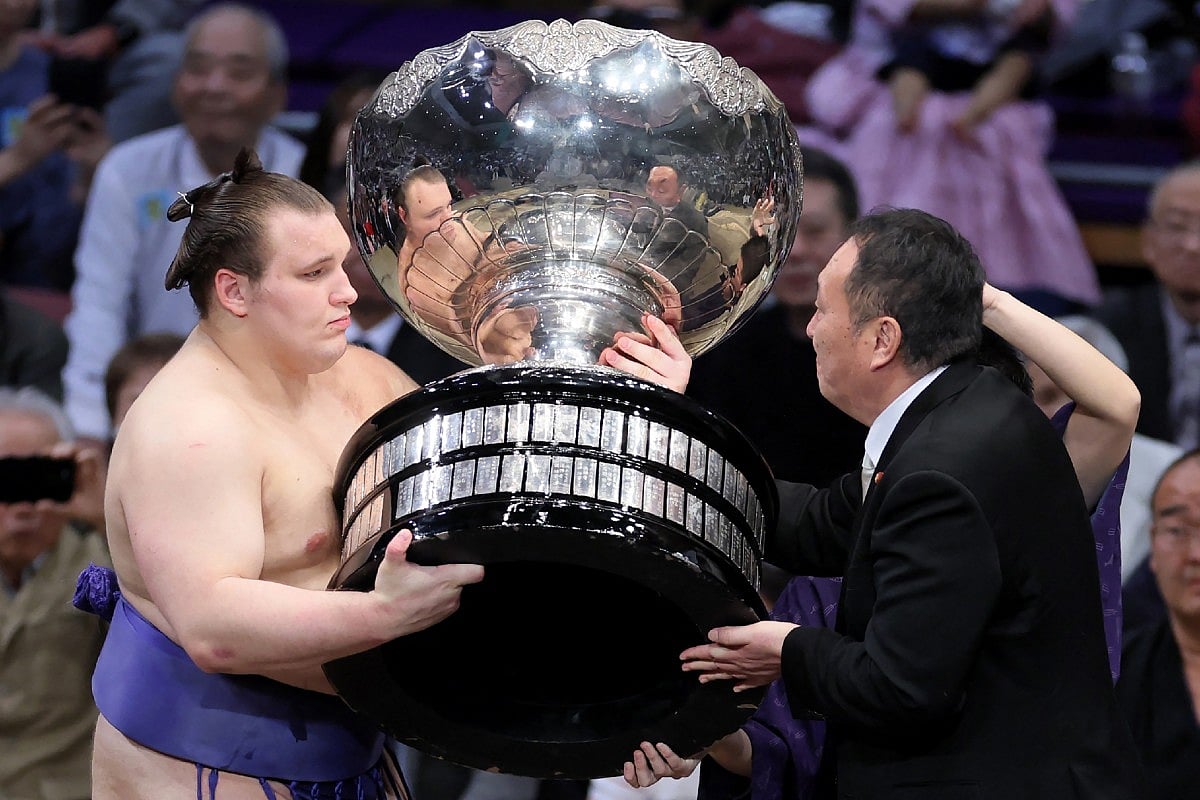 Ukrainian sumo wrestler Danylo Yavhusishyn, also known by his Japanese ring name Aonishiki Arata (L), receives the Prime Minister's Cup trophy after winning the Grand Sumo Tournament in Fukuoka on November 23, 2025.