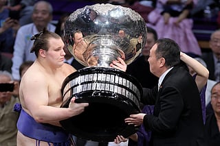 Ukrainian sumo wrestler Danylo Yavhusishyn, also known by his Japanese ring name Aonishiki Arata (L), receives the Prime Minister's Cup trophy after winning the Grand Sumo Tournament in Fukuoka on November 23, 2025.
