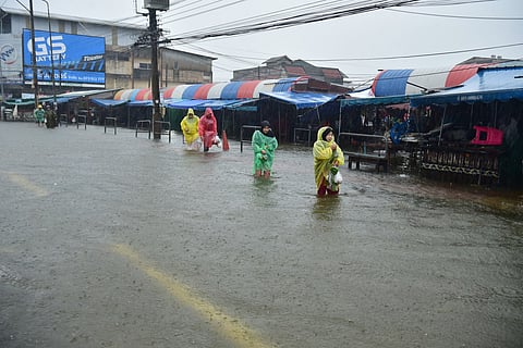 People wade through a flooded road beside a market following heavy rain in Thailand's southern province of Narathiwat on November 23, 2025.