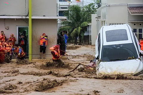 Rescuers wade through flood waters by holding a rope in their effort to evacuate residents who are trapped at their houses in Padang, West Sumatra province on November 27, 2025.