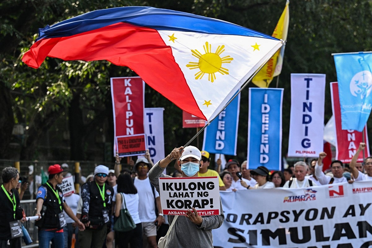 A protester with a Philippine flag marches with a placard that reads "jail all the corrupt" during an anti-corruption rally along Epifanio de los Santos Avenue, or EDSA, in Quezon City, Metro Manila on November 30, 2025.