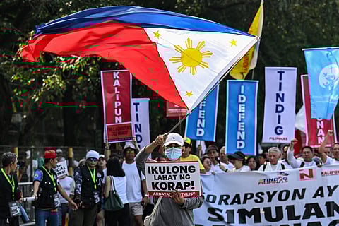 A protester with a Philippine flag marches with a placard that reads "jail all the corrupt" during an anti-corruption rally along Epifanio de los Santos Avenue, or EDSA, in Quezon City, Metro Manila on November 30, 2025.