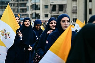 Lebanese Muslim women hold Vatican flags as they wait for the arrival of Pope Leo XIV in Beirut's southern suburbs, a packed residential area known as Dahiyeh, which is also a Hezbollah bastion, on November 30, 2025.