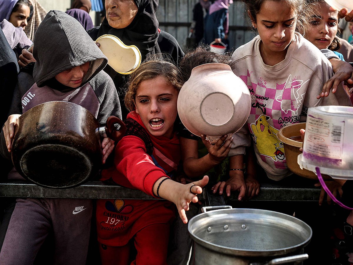 Displaced Palestinian children wait for food at a shelter where families have been living, in Nuseirat, in the central of Gaza Strip on November 23, 2025.