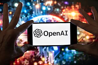 The OpenAI logo is seen displayed on a cell phone in front of an image on a computer screen generated by ChatGPT's Dall-E text-to-image model, Friday, Dec. 8, 2023, in Boston.
