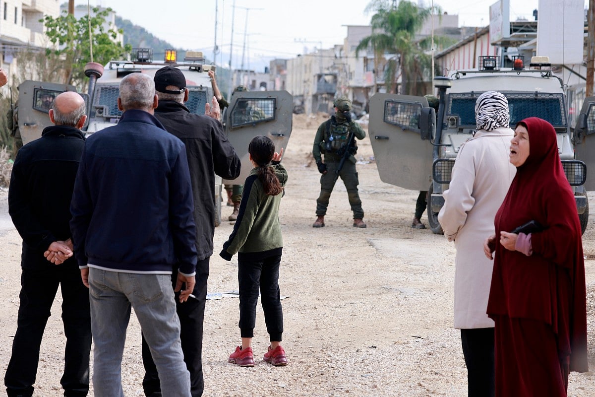Palestinians rally as Israeli soldiers block the entrance of the Nur Shams Palestinian refugee camp, in the Israeli-occupied northern West Bank on December 15, 2025, as they demand to be allowed back to their homes after the Israeli army expelled them and others in early 2025.