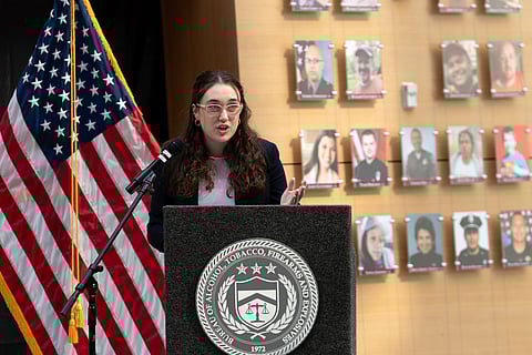 Survivor of gun violence Mia Tretta speaks while standing next to a wall with photographs of victims of gun violence during the Inaugural Gun Violence Survivors' Summit at ATF Headquarters in Washington, April 23, 2024. 