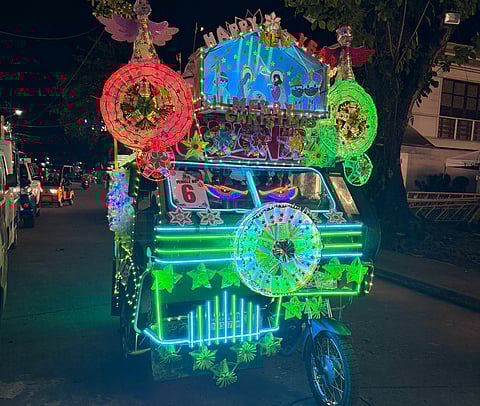 A tricycle, symbol of last-mile transport in the Philippines, twinkling with vibrant Christmas lights as it cruises through Gingoog, southern Philippines — pure holiday sparkle. The local plaza by the church glows like a "mini Disneyland," where decked-out trikes and park promise a glittering, merry visit full of festive cheer.