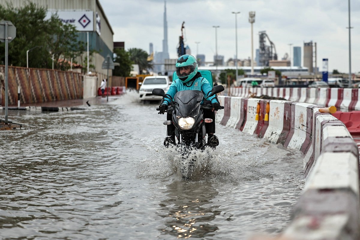 A man rides a motorbike lifting his feet to avoid getting them soaked, following heavy rains which left the street flooded, in Dubai.