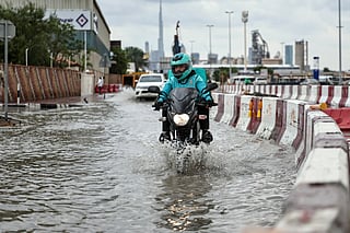 A man rides a motorbike lifting his feet to avoid getting them soaked, following heavy rains which left the street flooded, in Dubai.