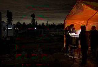 Leticia Serafin (2nd R) cooks tamales with her husband Paul Fonseca (L) and friend Pedro Jimenez, who holds up his phone light, ahead of the atmospheric river storm on December 23, 2025 in Altadena, California.