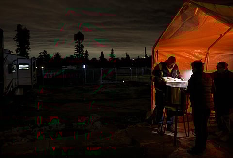Leticia Serafin (2nd R) cooks tamales with her husband Paul Fonseca (L) and friend Pedro Jimenez, who holds up his phone light, ahead of the atmospheric river storm on December 23, 2025 in Altadena, California.