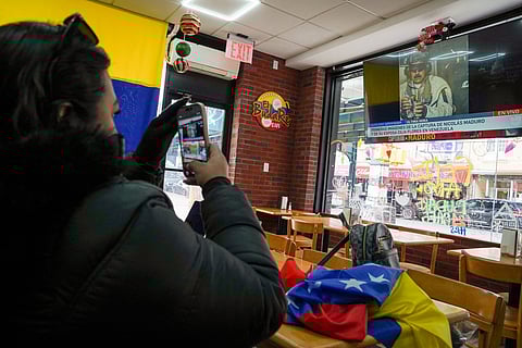 A woman takes a photograph of the television in El Budare Café after President Donald Trump posted a photo of Venezuelan leader Nicolás Maduro aboard the USS Iwo Jima heading for New York, where he faced charges in Manhattan federal court, on January 3, 2026 in the Queens borough of New York City.