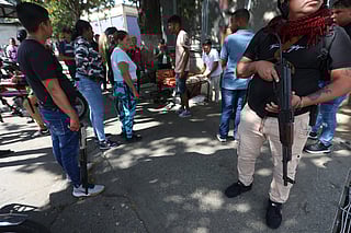 An armed supporter of ousted Venezuelan President Nicolas Maduro stands guard as he monitors vendors from speculating on goods prices in Caracas on January 4, 2026, one day after he was captured in a U.S. raid.