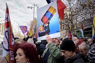 A protestor holds a caricature of US President Donald Trump drinking from a Venezuelan oil barrel by Portuguese cartoonist Vasco Gargalo, during a demonstration against the US operation in Venezuela to capture Venezuelan President, in front of the US Embassy in Madrid on January 4, 2026.