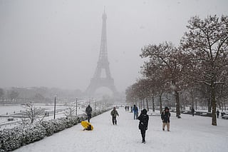 Pedestrians walk on snow at the Trocadero gardens with the the Eiffel Tower in the background during a snowfall in Paris on January 7, 2026.