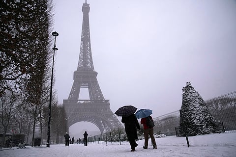 People walk near the Eiffel Tower during a snowfall Wednesday, Jan. 7, 2026 in Paris. (AP Photo/Christophe Ena)