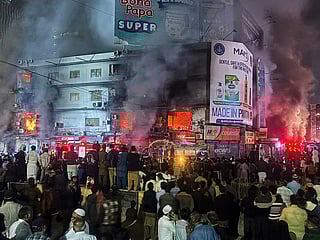 People gather as firefighters try to control a massive  fire that broke out in a multi-story shopping mall, in Karachi, Pakistan, Sunday, Jan. 18, 2026. 