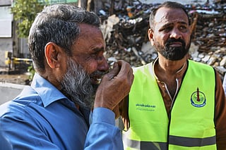 A rescue worker, right, stands next to a family member of a missing person, who waits near the site of a burnt building of a multi-story shopping plaza following a massive fire in Karach.