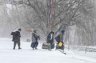 People with their belongings walk along a road during snowfall in Shibar area of the Sheikh Ali district of Afghanistan's Parwan province on January 21, 2026.