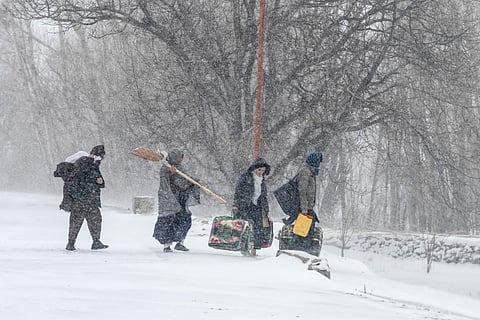 People with their belongings walk along a road during snowfall in Shibar area of the Sheikh Ali district of Afghanistan's Parwan province on January 21, 2026.