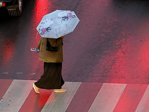 A resident crosses a street under a light drizzle in Sharjah on Sunday evening.