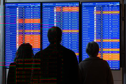 Travelers look at a flight status board as flights are delayed and cancelled.