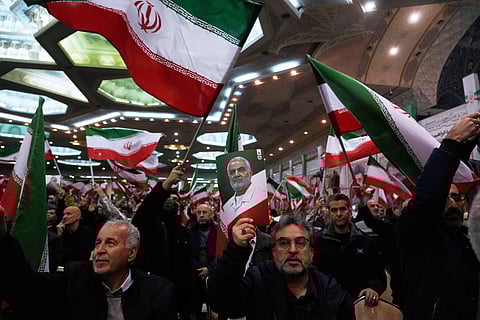 People wave Iranian flags as one of them holds up a poster of the late commander of the Iran's Revolutionary Guard expeditionary Quds Force, Gen. Qassem Soleimani, who was killed in a U.S. drone attack in 2020.