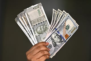 Indian rupee and US dollar currency notes are held by a foreign exchange employee at an office in New Delhi on August 26, 2025.