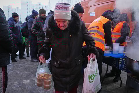 An elderly woman carries her bags out of a hot food distribution point during a power outage caused by Russia's repeated air strikes on the country's power grid, in Kyiv, Ukraine, Monday, Feb. 2, 2026. (AP Photo/Sergey Grits)