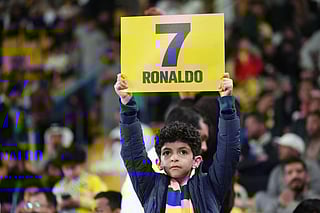 A young supporter holds a placard showing the name of Cristiano Ronaldo ahead of the Saudi Pro League football match between Al-Nassr and Al-Ittihad at Al-Awwal Park Stadium