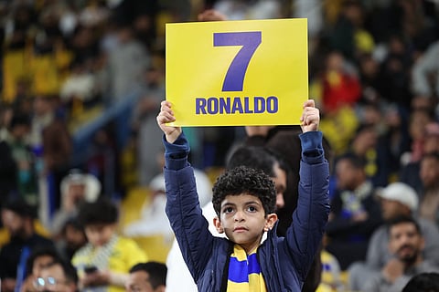 A young supporter holds a placard showing the name of Cristiano Ronaldo ahead of the Saudi Pro League football match between Al-Nassr and Al-Ittihad at Al-Awwal Park Stadium