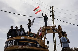 Standing on a digger used to clear the rubble of destroyed homes and businesses, a Lebanese youth holds up the Lebanese flag as residents wait for the arrival of Lebanon's prime minister during his visit to the heavily-damaged southern village of Kfar Shouba, near the border with Israel on February 8, 2026.