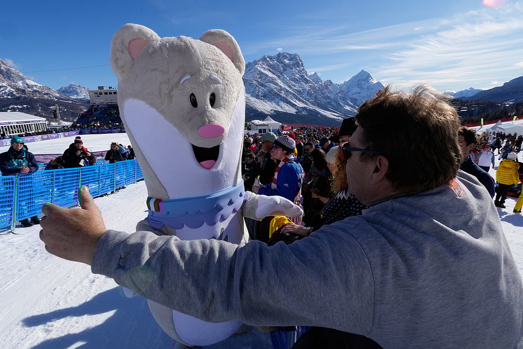 A spectator moves in to hug Olympic mascot Tina prior to an alpine ski women's downhill race, at the 2026 Winter Olympics, in Cortina d'Ampezzo, Italy, Sunday, Feb. 8, 2026.. (AP Photo/Robert F. Bukaty)