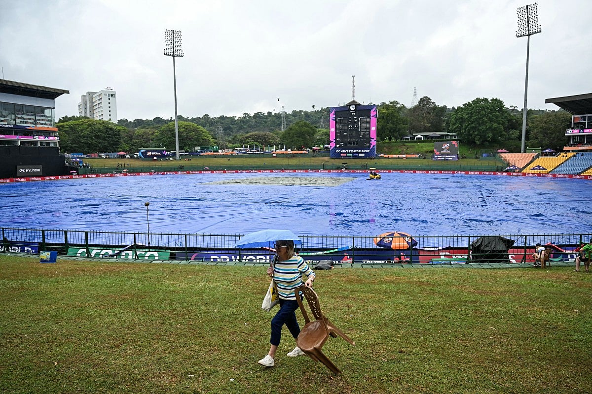 A cricket fan carrying an umbrella walks past the covered pitch as rain delays the start of the 2026 ICC Men's T20 Cricket World Cup group stage match between Zimbabwe and Ireland at Pallekele International Cricket Stadium in Kandy on February 17, 2026.
