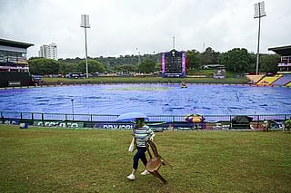 A cricket fan carrying an umbrella walks past the covered pitch as rain delays the start of the 2026 ICC Men's T20 Cricket World Cup group stage match between Zimbabwe and Ireland at Pallekele International Cricket Stadium in Kandy on February 17, 2026.