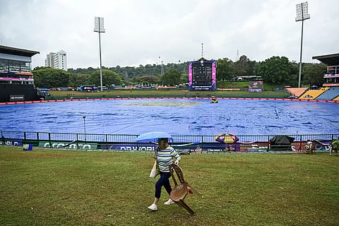 A cricket fan carrying an umbrella walks past the covered pitch as rain delays the start of the 2026 ICC Men's T20 Cricket World Cup group stage match between Zimbabwe and Ireland at Pallekele International Cricket Stadium in Kandy on February 17, 2026.