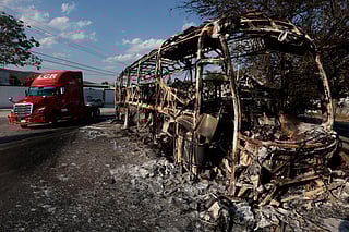 A truck unit passes by a burned bus, allegedly set on fire by organised crime groups in response to an operation to arrest a high-priority security target, on a highway near Acatlan de Juarez, Jalisco state, Mexico on February 22, 2026.