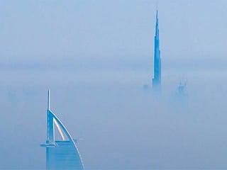 Burj Khalifa and the distinctive silhouette of the Burj Al Arab rising above a thick layer of white mist.