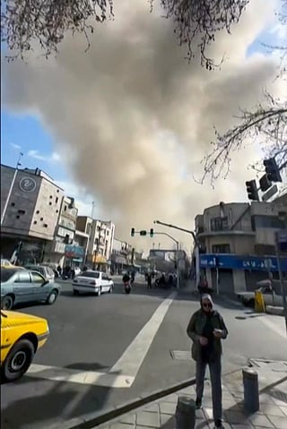 This video grab taken from UGC images posted on social media on February 28, 2026, and verified by AFPTV teams in Paris, shows a man walking as a plume of smoke rises following a repoted explosion in Tehran.