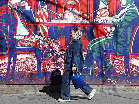An Iranian woman walks past an anti-US mural featuring Iran-US talks, next to the former US embassy in Tehran on February 26, 2026. 