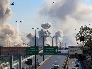 Motorists drive along an expressway as plumes of smoke rise after a strike in Tehran.
