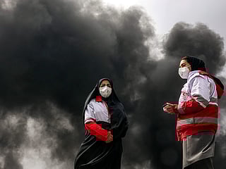 Women members of Iran's Red Crescent society stand near smoke plumes from an ongoing fire following an overnight airstrike on the Shahran oil refinery in northwestern Tehran. 
