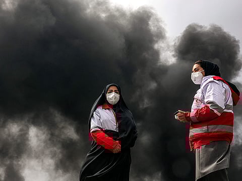 Women members of Iran's Red Crescent society stand near smoke plumes from an ongoing fire following an overnight airstrike on the Shahran oil refinery in northwestern Tehran. 