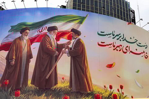 A banner is displayed at Valiasr Square in central Tehran on March 10, 2026, depicting Iran's late supreme leader Ayatollah Ruhollah Khomeini watching as his successor the late Ayatollah Ali Khamenei hands over a national flag to his son and new supreme leader Mojtaba Khamenei.