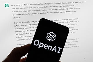 The OpenAI logo is displayed on a mobile phone in front of a computer screen with output from ChatGPT, March 21, 2023, in Boston. 