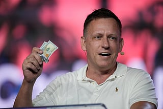 FILE - Peter Thiel, co-founder of PayPal and Palantir, offers a pair of hundred dollar bills to attendees during a keynote address at the Bitcoin Conference, April 7, 2022, in Miami Beach, Fla. (AP Photo/Rebecca Blackwell, File)